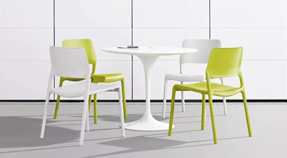 Vier Vitra HAL Stühle in Weiß und Grün um einen weißen runden Tisch auf grauem Boden vor einer weißen Wand.