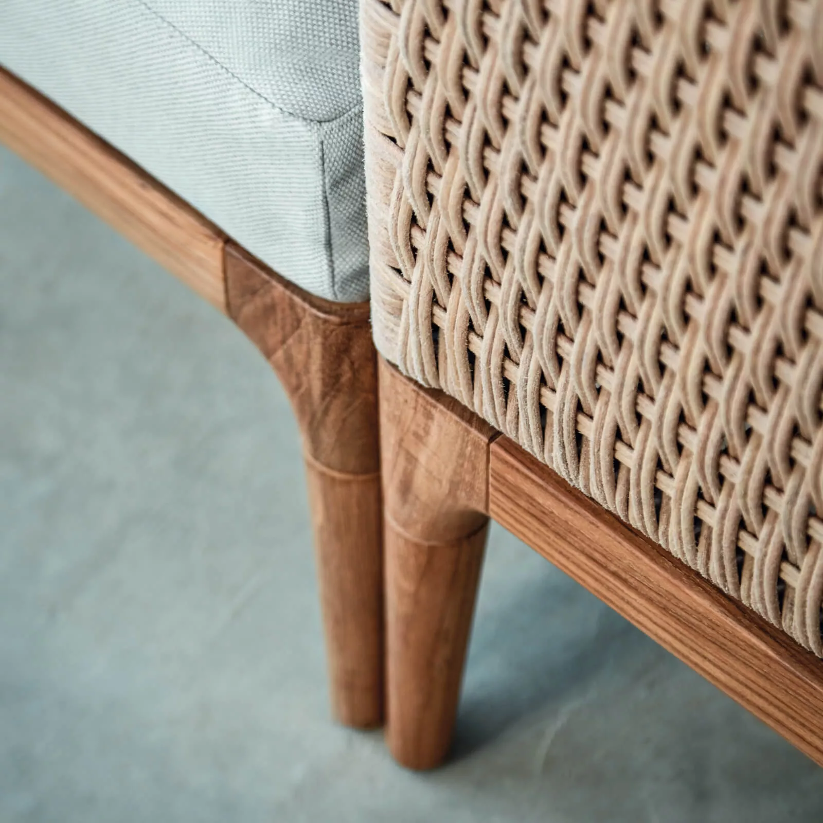 Gloster Lima Lounge in Beige und Holz, Detailansicht der geflochtenen Textur und Holzbeine auf grauem Hintergrund.