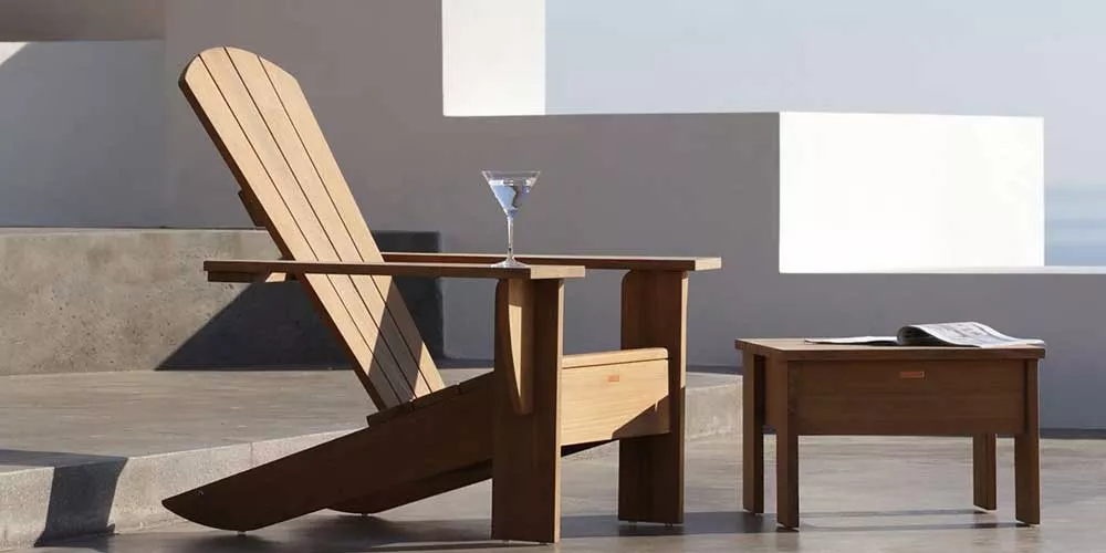 Royal Botania New England Gartenmöbel in Holzoptik, bestehend aus einem Sessel und einem Tisch, auf einer Terrasse mit Meerblick.