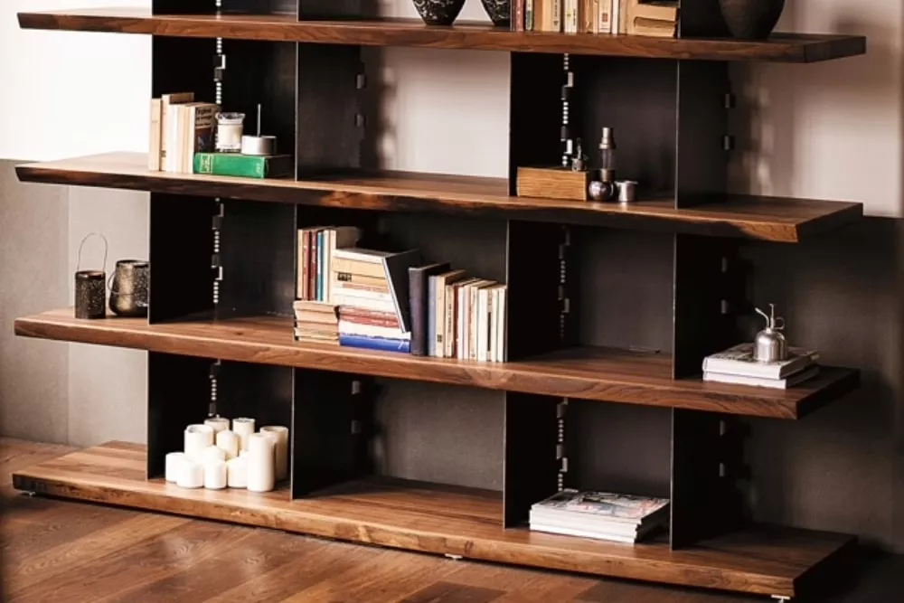 RIVA 1920 Regal aus dunklem Holz mit schwarzen Metallakzenten, gefüllt mit Büchern und Dekorationen, auf einem Holzboden vor einer weißen Wand.