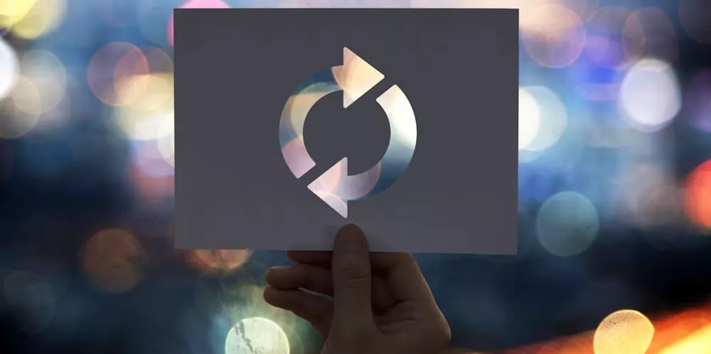 Hand hält ein Blatt mit einem Rückgabesymbol vor einem verschwommenen, bunten Hintergrund.