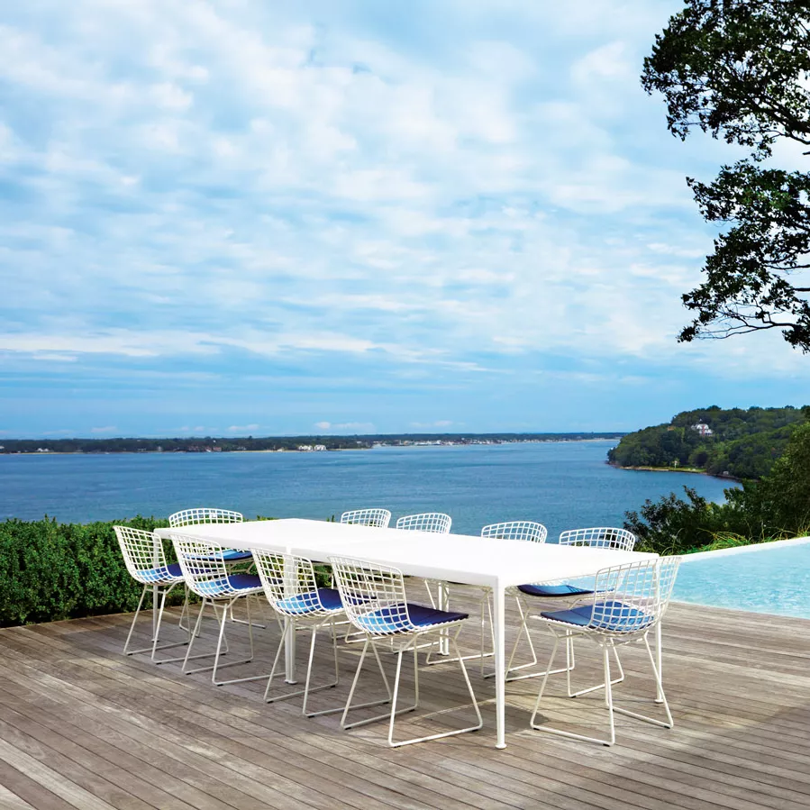Knoll Harry Bertoia Essplatzstuhl in Weiß an einem langen Esstisch auf einer Terrasse mit Blick auf das Meer