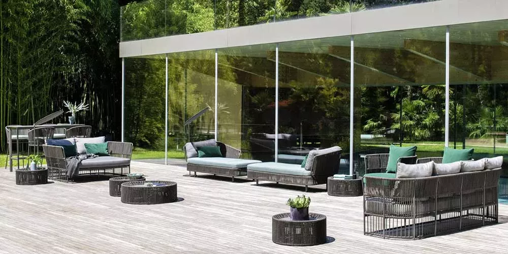 Varaschin Tibidabo Lounge Gartenmöbel in Grau auf einer Holzterrasse vor einem modernen Glaspavillon im Grünen.