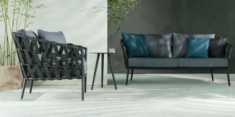 Vincent Sheppard Leo Outdoor-Sofa-Set in Dunkelgrau auf einer Terrasse mit Pflanzen im Hintergrund, stimmungsvolle Atmosphäre.