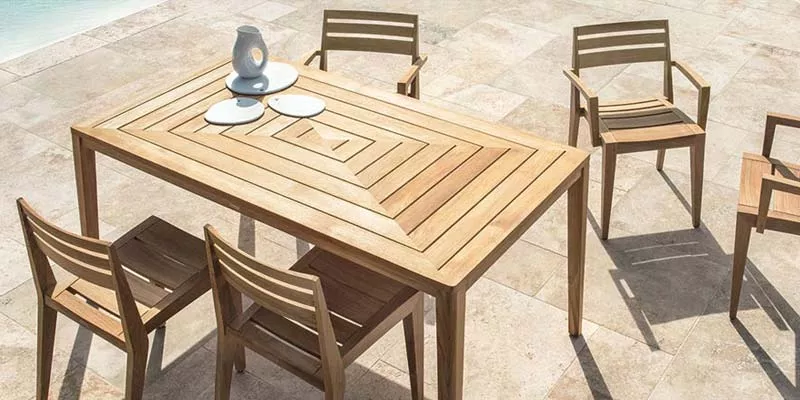 Ethimo Ribot Outdoor Essgruppe aus hellem Holz auf einer Terrasse mit Steinboden, bestehend aus einem Tisch und vier Stühlen.