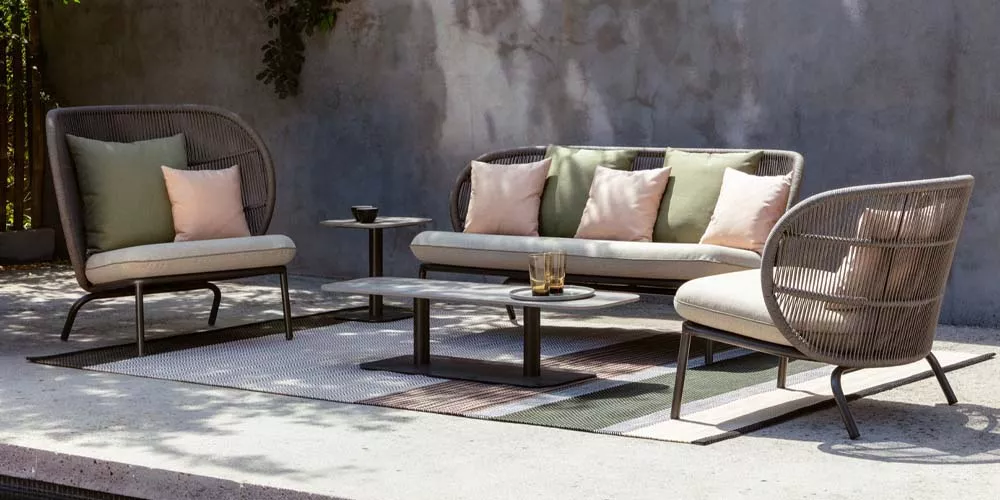 Vincent Sheppard Kodo Gartenmöbel-Set in Grau und Beige auf einer Terrasse mit Betonwand im Hintergrund, stimmungsvolles Ambiente.