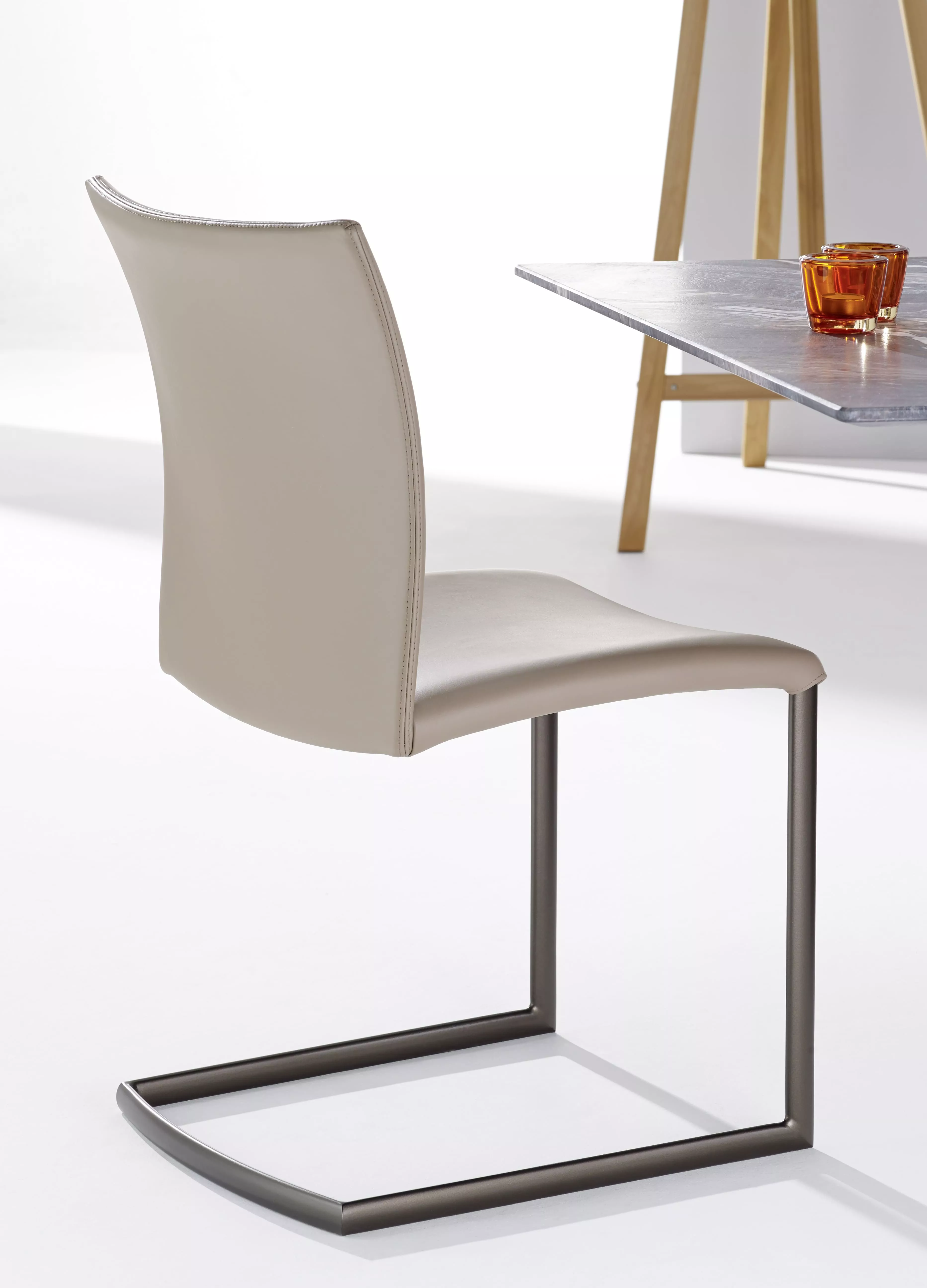 DRAENERT Nobile Swing Soft ohne Armlehne in Beige an einem Tisch mit einem orangefarbenen Glas auf einer weißen Fläche