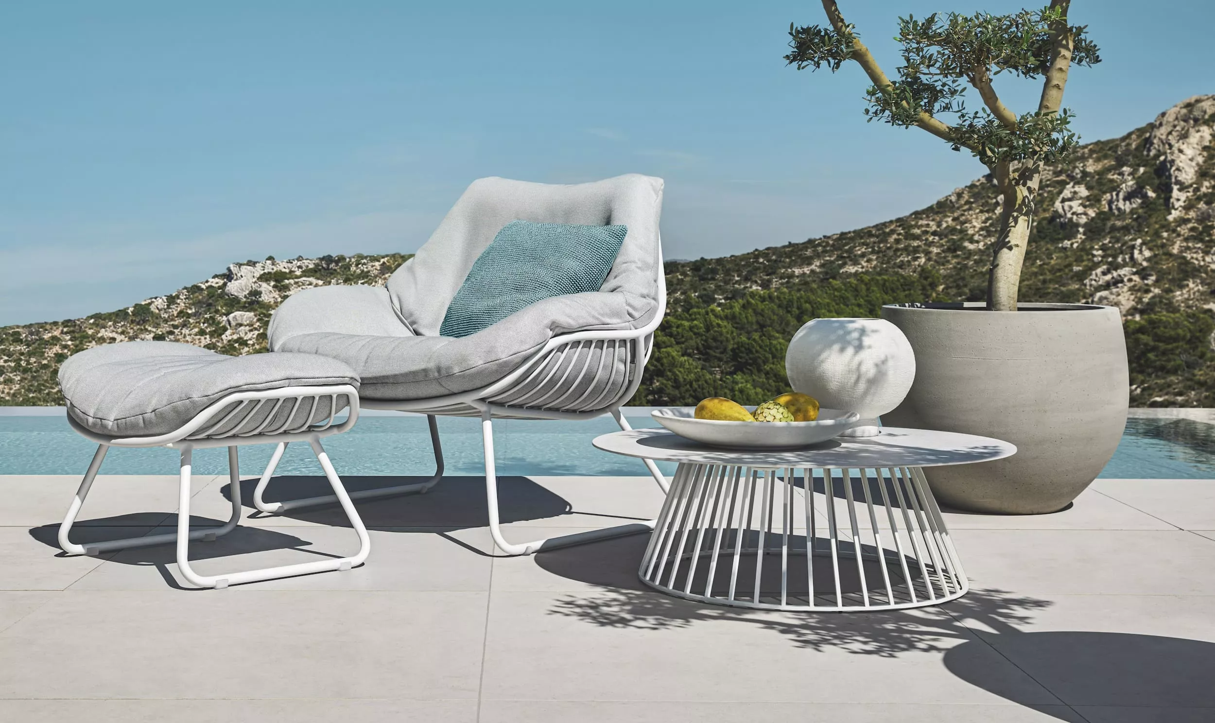 Solpuri Chill-A Sessel mit Hocker und Beistelltisch auf einer Terrasse mit Blick auf Berge und Pool im Hintergrund Moodbild