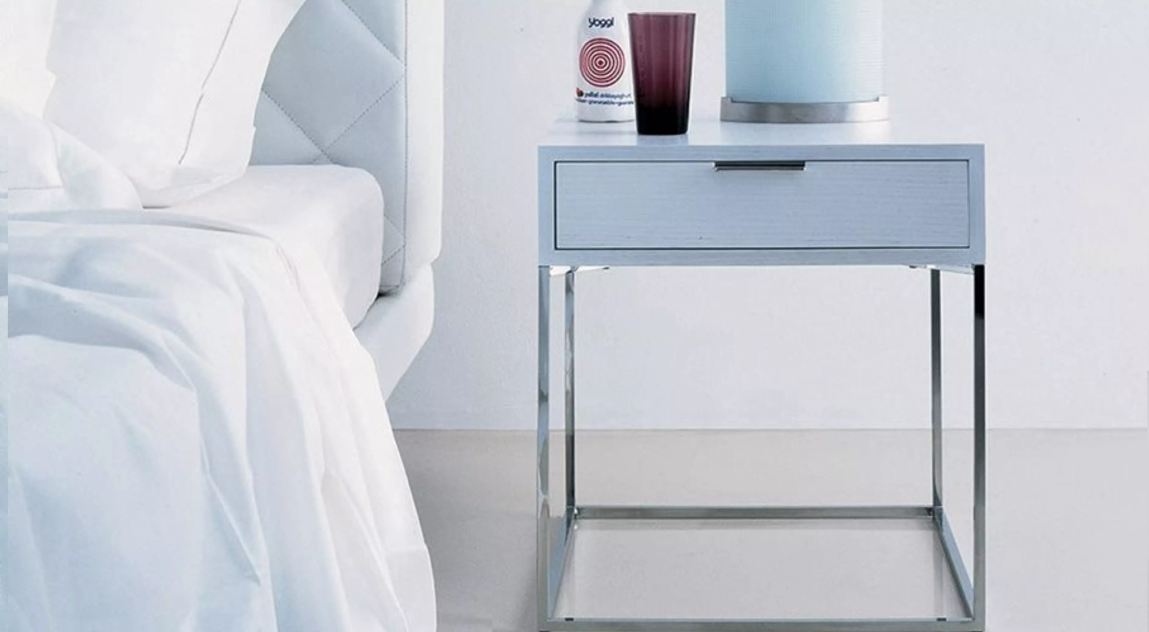 Oscar Nachttisch in Weiß mit Metallgestell, abgebildet in einem modernen Schlafzimmer auf hellem Boden.