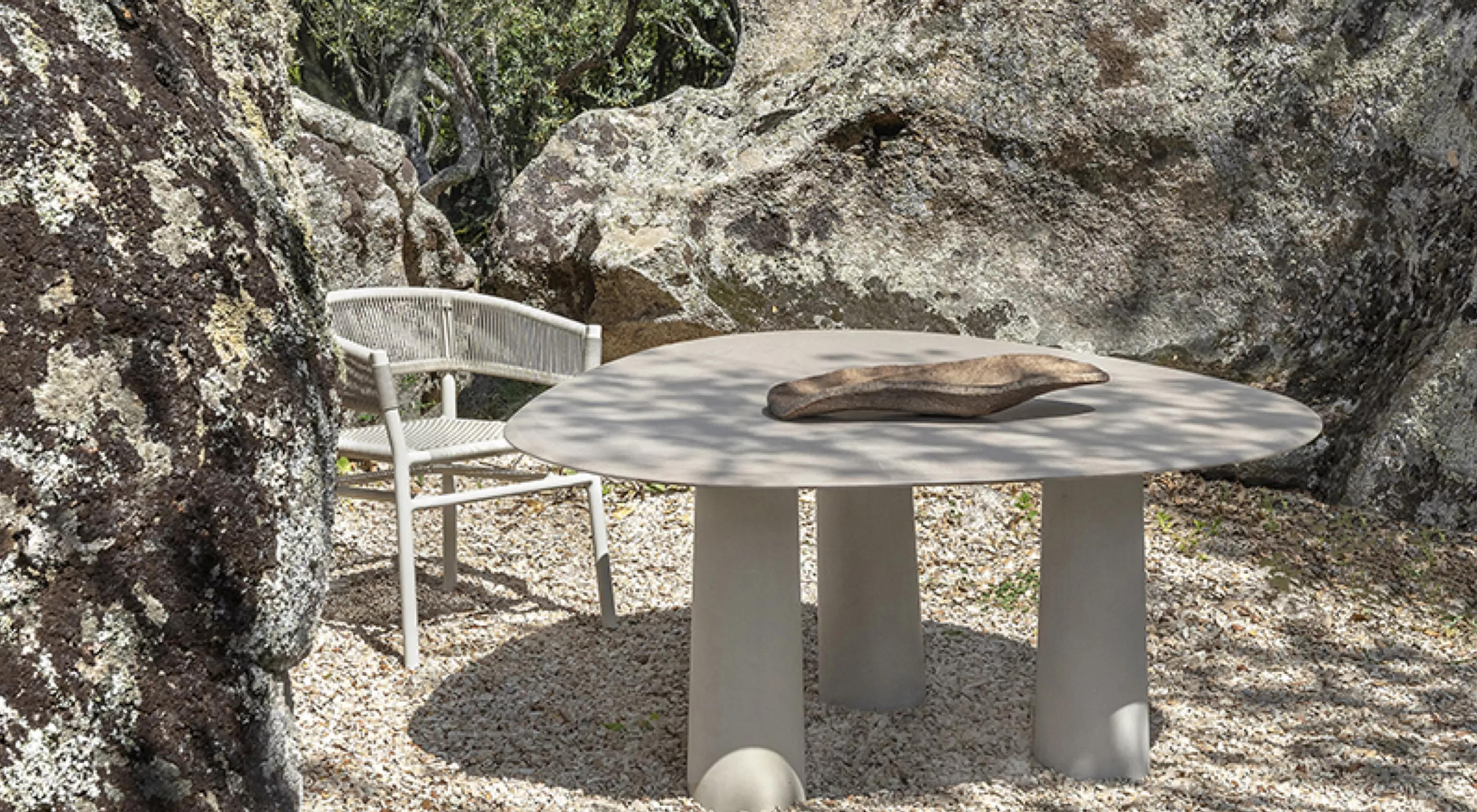 Runder, beiger Tisch von Villa Schmidt auf Kiesboden zwischen Felsen, mit passendem Stuhl, in natürlicher Umgebung fotografiert.