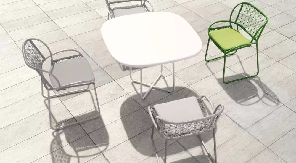 Kenneth Cobonpue Adesso Essgruppe mit weißem Tisch und grauen sowie einem grünen Stuhl auf Steinboden in Vogelperspektive.