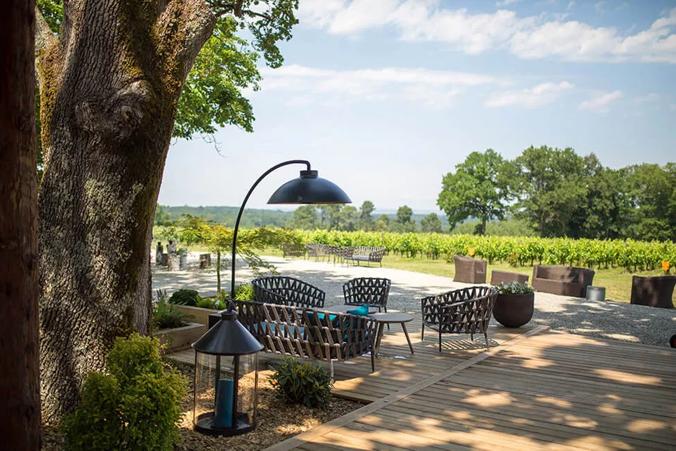 Heatsail Dome Arc Stehlampe in Schwarz auf einer Terrasse mit Blick auf einen Weinberg, umgeben von modernen Gartenmöbeln.