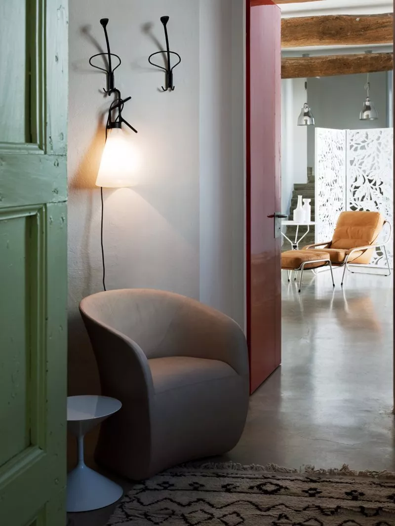 Ein gemütlicher Raum mit einem Zanotta 873 Calla Sessel und einem Beistelltisch neben einer Lampe an der Wand im Hintergrund ein Essbereich.