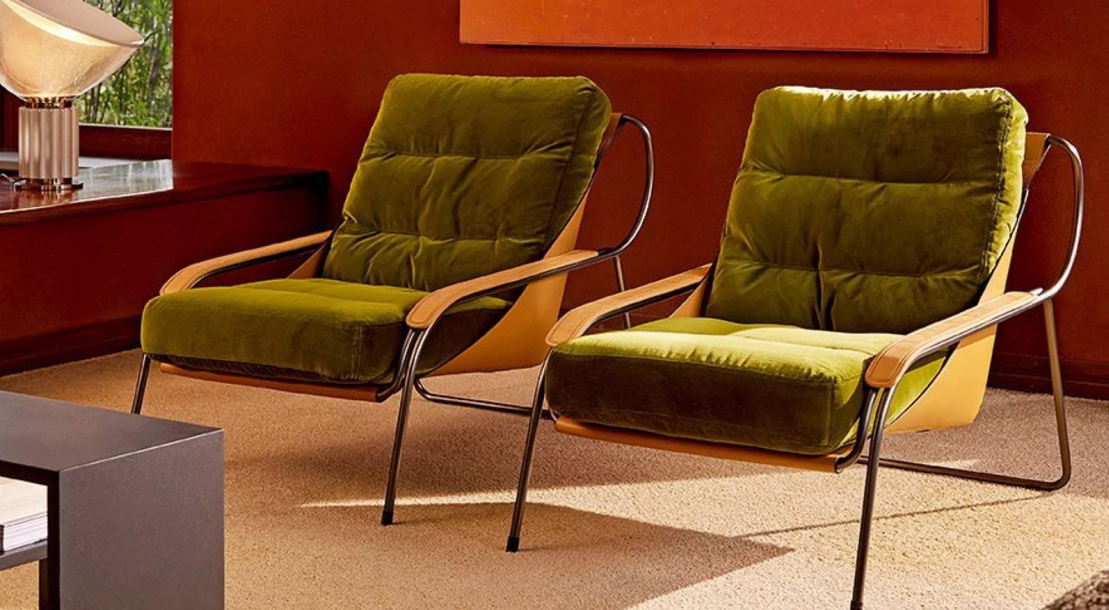 Zwei grüne MAGGIOLINA Sessel mit Metallrahmen und Holzarmlehnen auf beigem Teppich vor einer roten Wand in einem modernen Wohnzimmer.