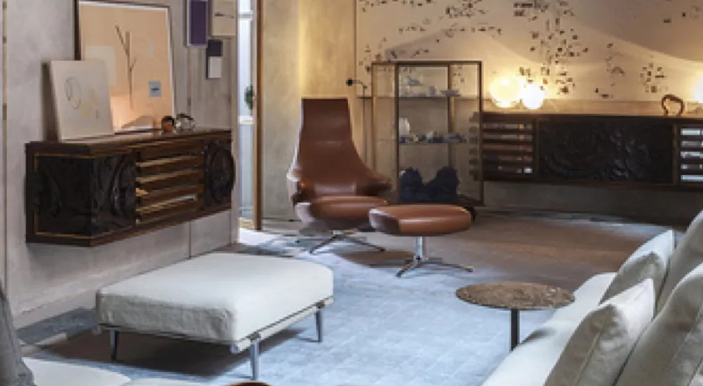 Gemütliches Wohnzimmer mit braunem Ledersessel und Hocker, hellem Sofa und moderner Kunst an der Wand, stimmungsvolle Beleuchtung.