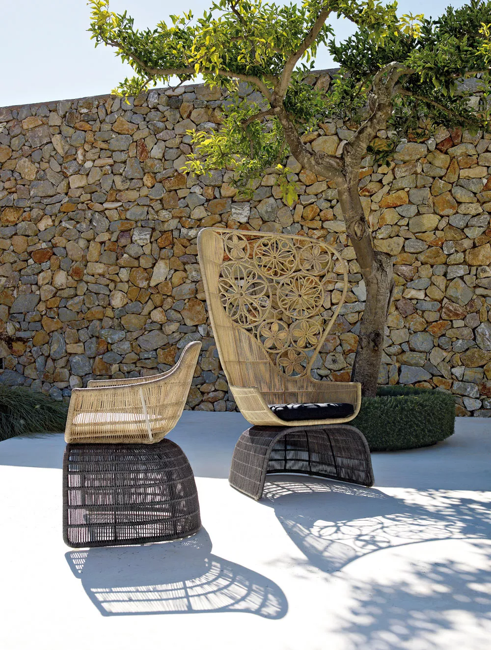 B&B Italia Crinoline Outdoor Loungegruppe bestehend aus zwei geflochtenen Sesseln auf einer Terrasse vor einer Steinmauer und einem Baum