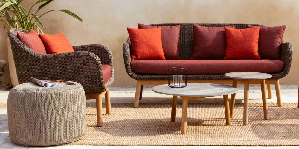 Vincent Sheppard Anton Gartenmöbel-Set in Braun und Rot auf einer Terrasse mit beigem Hintergrund und Pflanzen im Hintergrund.