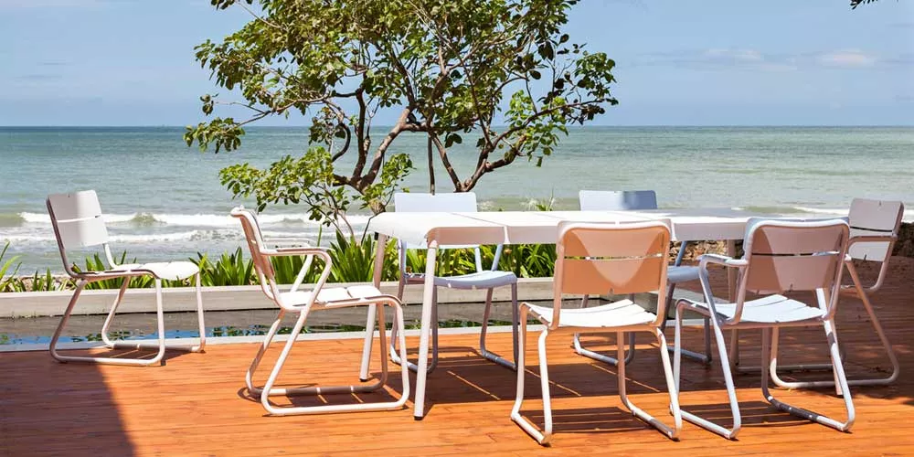 Oasiq Corail Essgruppe in Weiß auf Holzterrasse mit Meerblick, bestehend aus Tisch und acht Stühlen, ideal für Gartenmöbel.