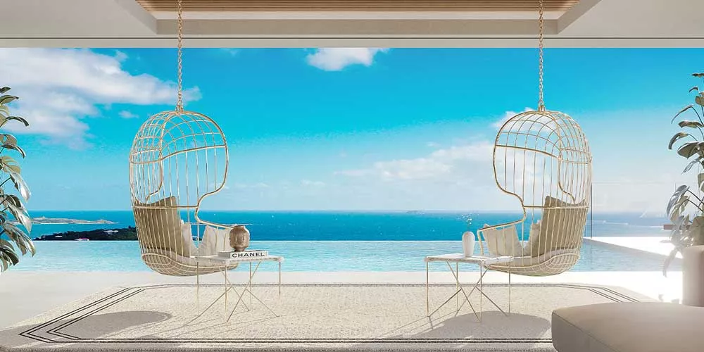 Zwei weiße Mayface Nodo Lounge-Sessel aus Metall mit Kissen, auf einer Terrasse mit Meerblick, unter blauem Himmel.