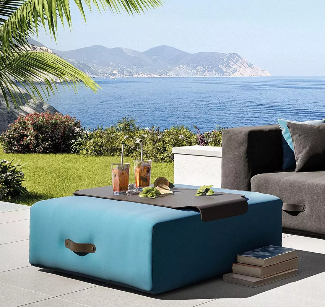 Conmoto Miami Tablett auf türkisfarbenem Loungehocker im Garten, 92x92 cm, mit Meerblick im Hintergrund.