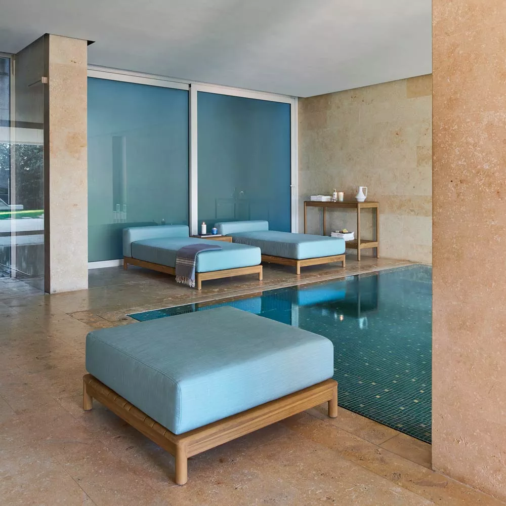 Varaschin Barcode Loungehocker mit Teakholzgestell in Blau, in modernem Innenraum mit Pool und Steinwänden.