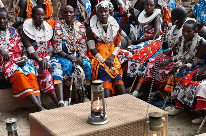 Eine Gruppe von Menschen in traditioneller Kleidung sitzt um einen Tisch im Freien mit Laternen darauf und unterhält sich.