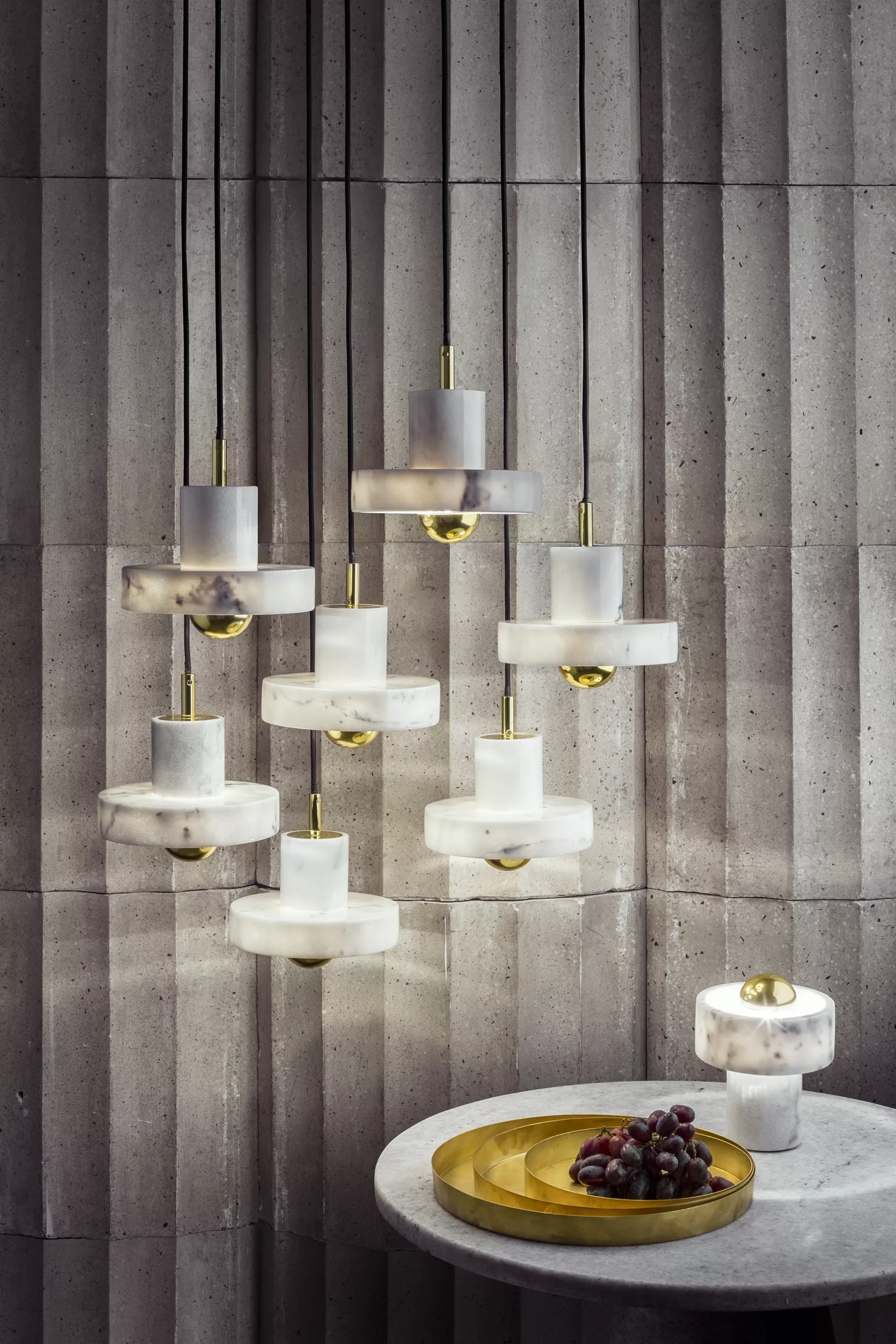 Tom Dixon Stone Pendant Light, weiße Marmor-Hängeleuchte, in modernem Ambiente vor einer Betonwand, mit goldenen Akzenten.