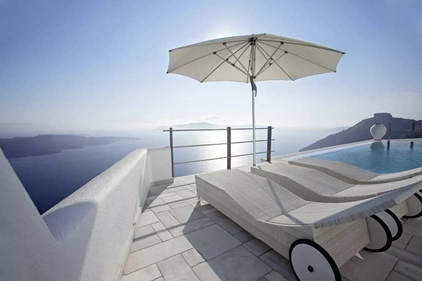 Weißer Glatz Sonnenschirm Fortino auf einer Terrasse mit Meerblick, neben zwei weißen Liegestühlen am Pool.