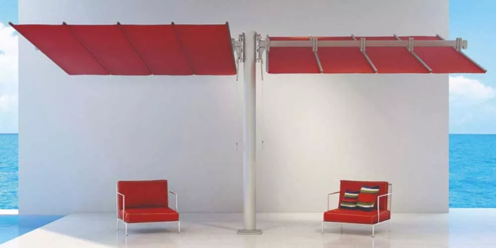 Zwei rote FIM Flexy Twin Sonnenschirme auf einer Terrasse mit Meerblick, flankiert von zwei roten Sesseln.
