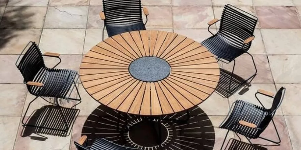 Sechs schwarze HOUE Circle Stühle um einen runden Holztisch auf einer Steinplatte, Vogelperspektive, sonnige Terrasse.