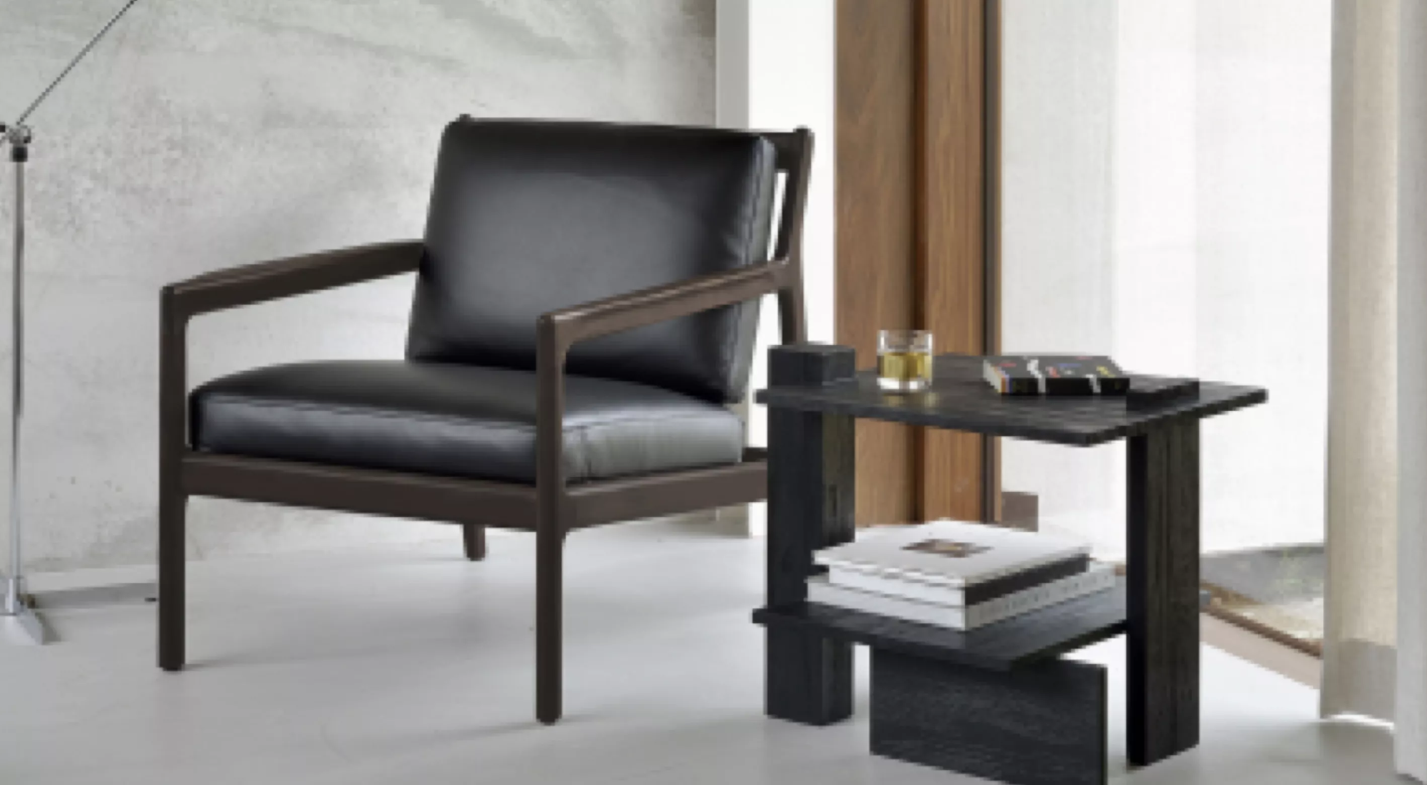 Schwarzer Walter Knoll Vostra Sessel in modernem Wohnzimmer mit grauer Wand und Holztisch, auf dem Bücher und ein Glas stehen.