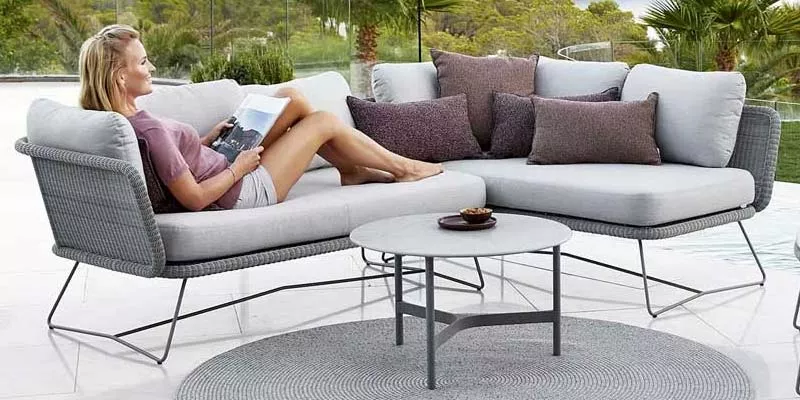 Frau entspannt auf grauem Cane-line Horizon Lounge-Set mit Kissen, im Freien auf Terrasse mit grünem Hintergrund.