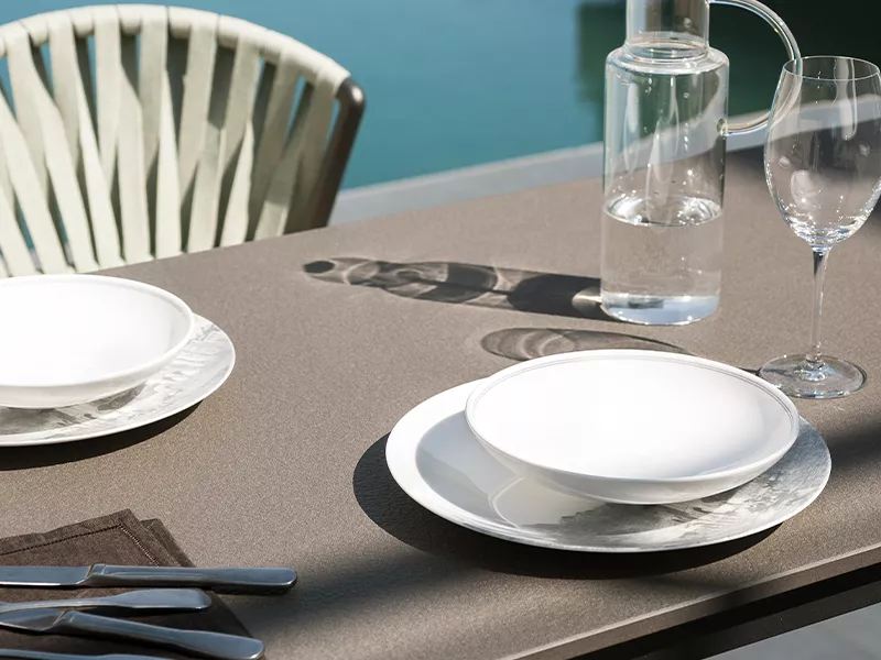 Outdoor-Küche von Roda Norma in Braun, gedeckter Tisch mit weißem Geschirr und Gläsern, im Hintergrund ein Pool.