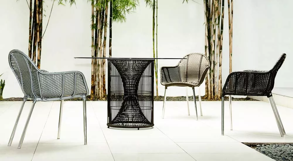 Kenneth Cobonpue Amaya Essgruppe in Schwarz und Grau, bestehend aus einem Tisch und drei Stühlen, auf einer Terrasse mit Bambushintergrund.