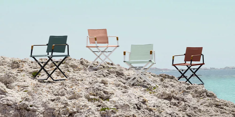 Vier Dedon Seax Stühle in verschiedenen Farben stehen auf einem Felsen am Meer unter klarem Himmel