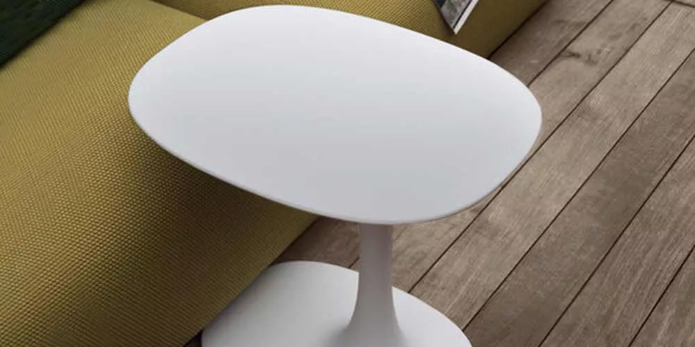 B&B Italia AVA Outdoor Beistelltisch in Weiß auf einer Holzterrasse neben einem grünen Sofa