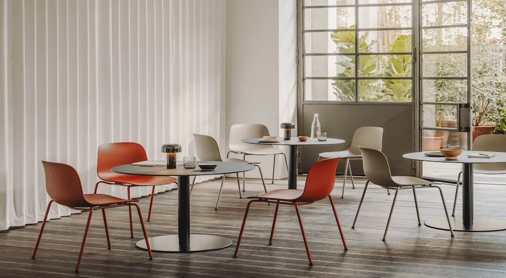 Stimmungsbild eines modernen Cafés mit Vitra Rondo Stühlen in Rot und Beige vor einer Fensterfront und weißen Vorhängen.