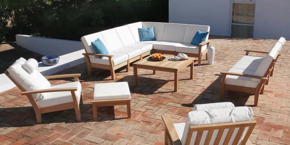 Barlow Tyrie Heaven Loungegruppe in hellem Holz mit weißen Polstern und blauen Kissen auf einer Terrasse mit Ziegelboden.