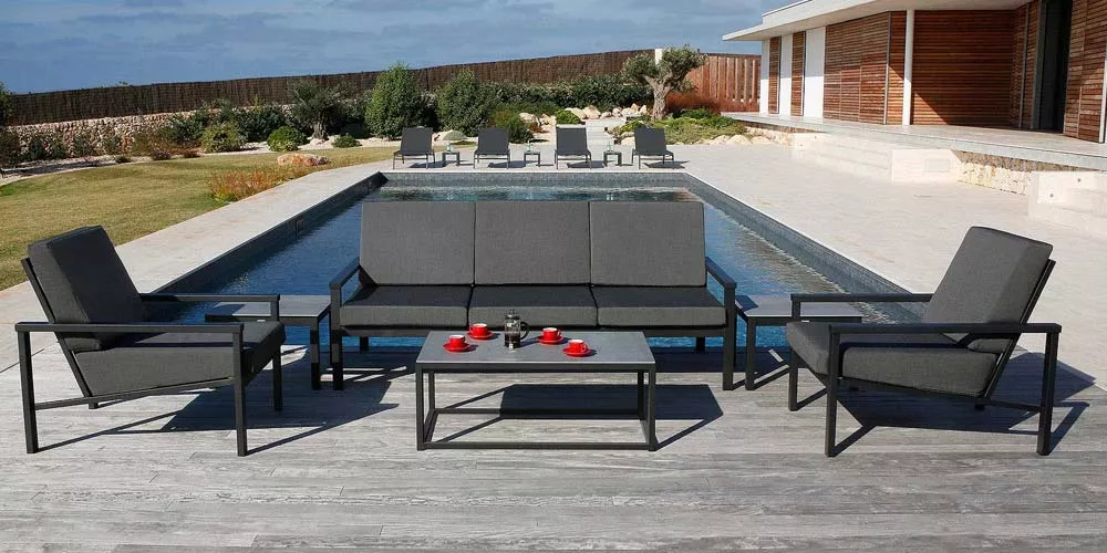 Barlow Tyrie Equinox Loungegruppe in Anthrazit auf einer Terrasse mit Pool im Hintergrund, bestehend aus Sofa, Sesseln und Tisch.