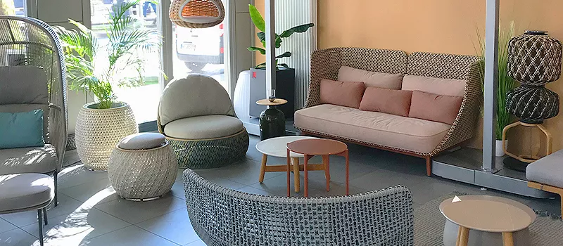 Gemütliche Gartenmöbel-Ausstellung mit verschiedenen Sitzgelegenheiten in neutralen Tönen, umgeben von Pflanzen in einem hellen Raum.