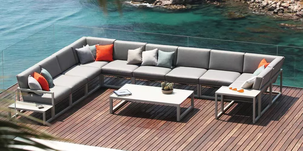 Royal Botania Ninix Loungegruppe in Grau auf Holzterrasse mit Meerblick, dekoriert mit bunten Kissen, stimmungsvolles Outdoor-Setting.