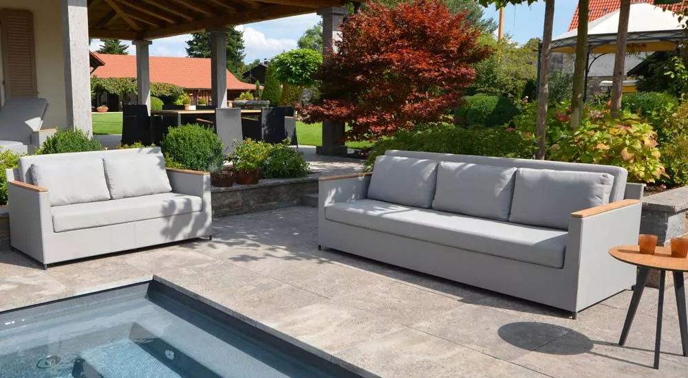 Fischer Möbel Rio Loungegruppe in hellgrau auf einer Terrasse mit Gartenblick, bestehend aus einem Sofa und einem Zweisitzer.