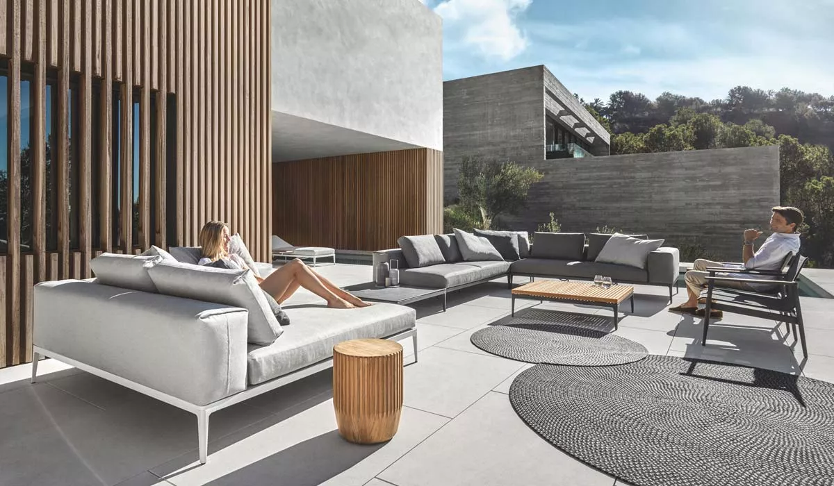 Gloster Grid Gartenmöbel Loungegruppe in Grau auf moderner Terrasse mit Holz- und Betonakzenten, entspannte Atmosphäre.