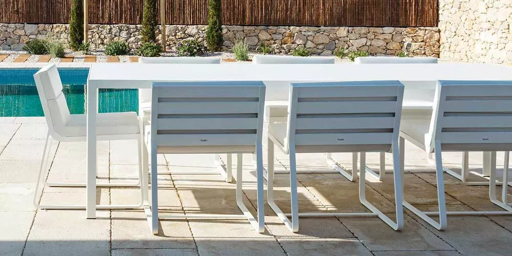 Bivaq Dats Essgruppe in Weiß, Gartenmöbel-Set mit modernem Design, auf einer Terrasse neben einem Pool vor einer Steinmauer.