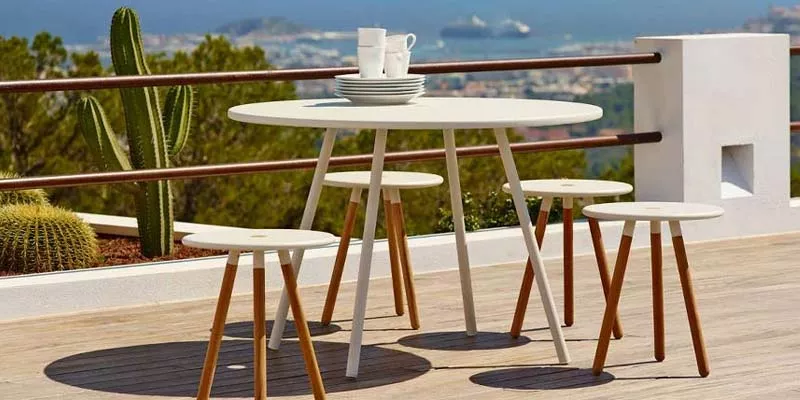 Cane-line Area Essgruppe in Weiß auf einer Terrasse mit Meerblick, bestehend aus einem runden Tisch und drei Hockern.