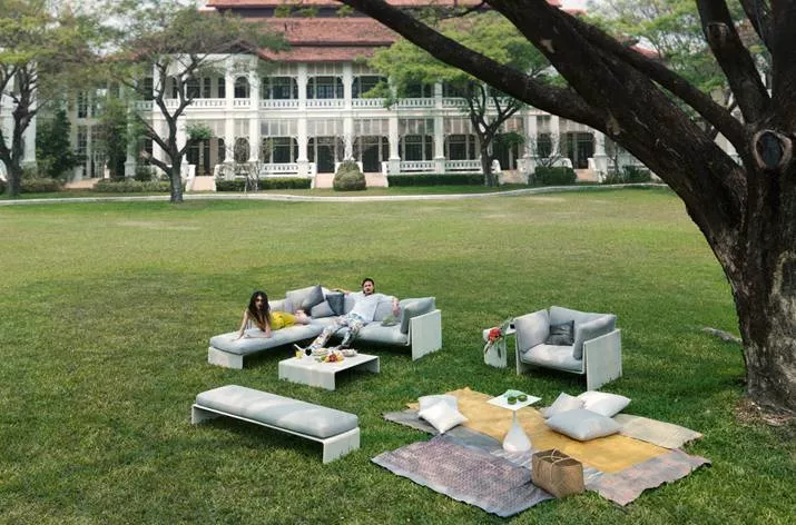 Dedon Slim Line Kollektion und Dedon Panama Gartenmöbel auf einer Wiese vor einem großen Gebäude zwei Personen entspannen auf den Möbeln