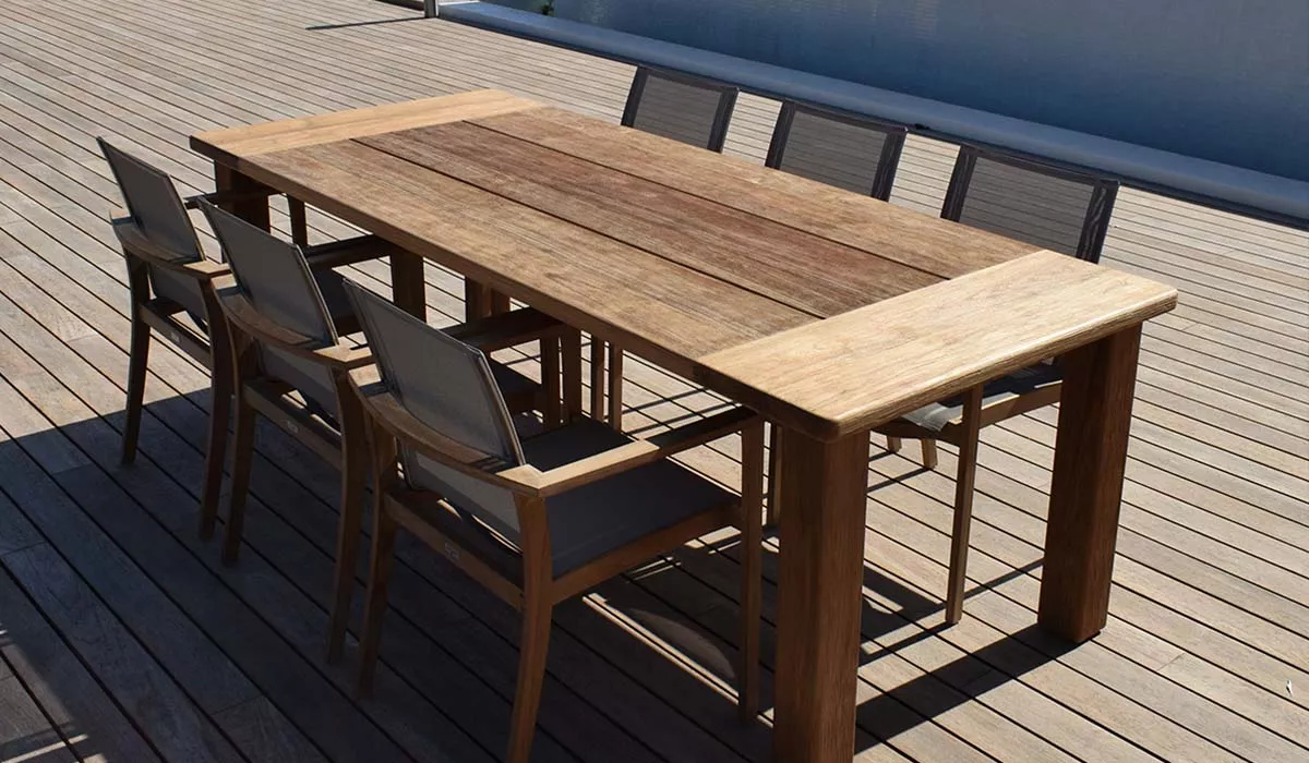 Royal Mirage Tisch aus hellem Holz auf einer Terrasse mit Blick auf das Wasser, umgeben von sechs passenden Stühlen.