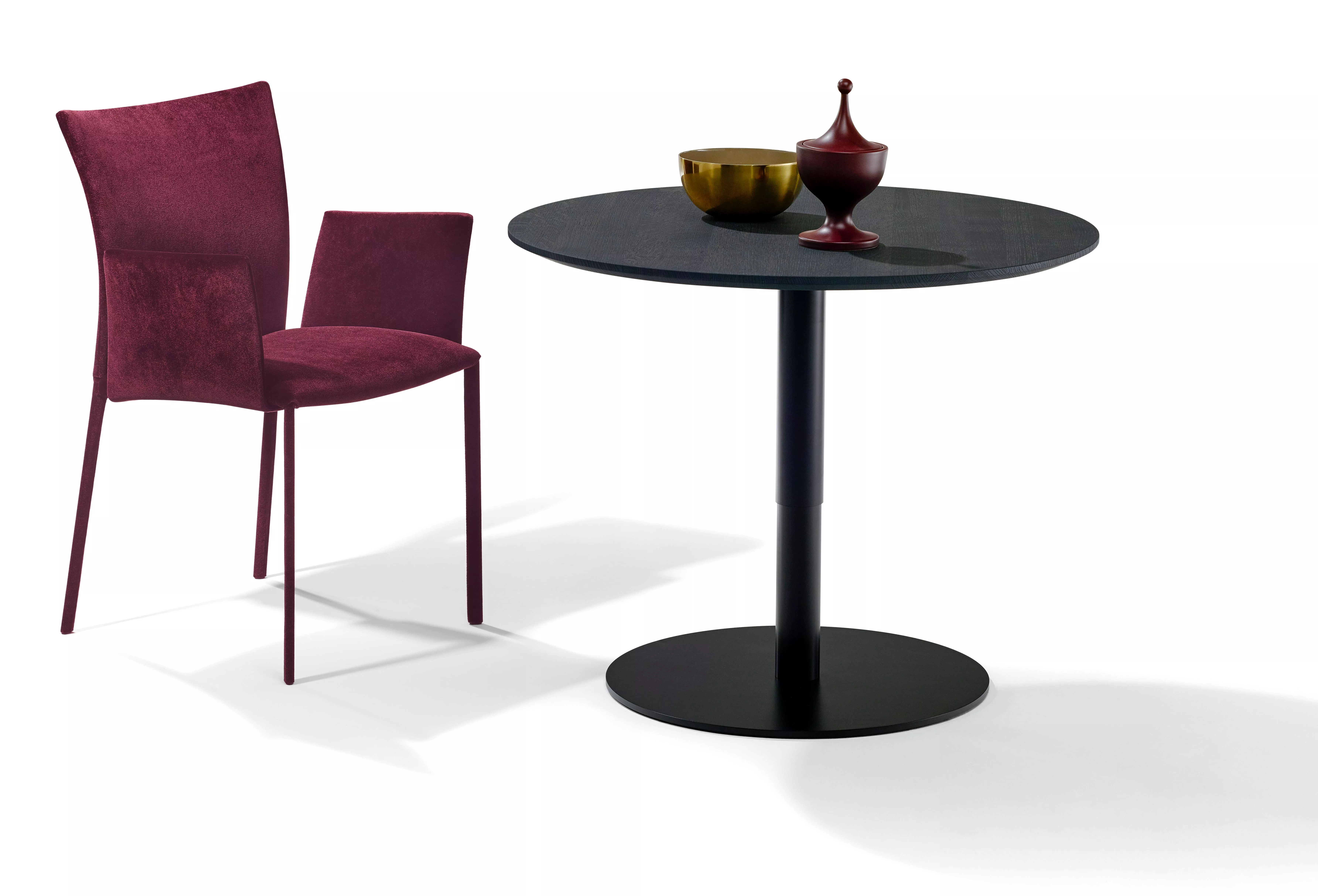 Ein DRAENERT Nobile Soft Stuhl in Rot steht neben einem runden schwarzen Tisch mit zwei dekorativen Schalen auf weißem Hintergrund.