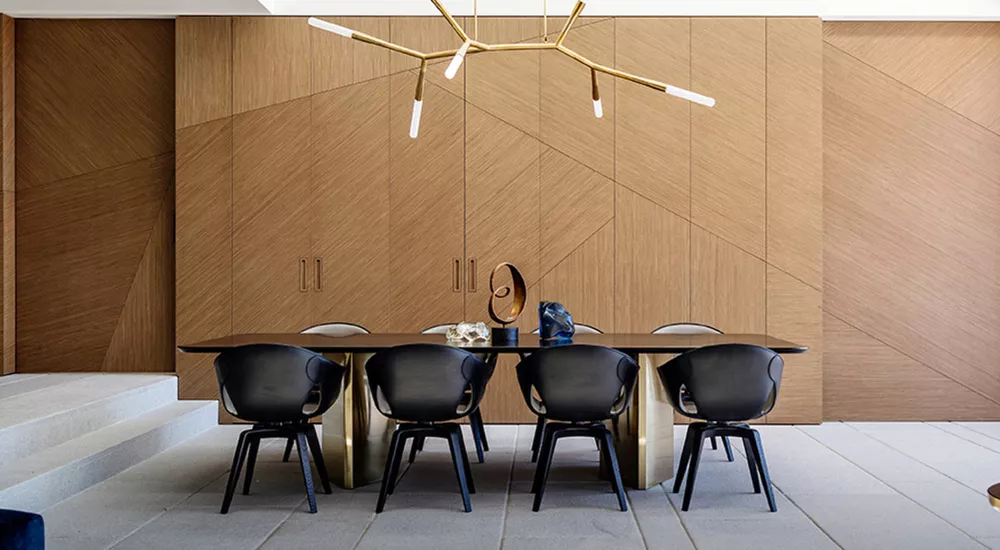 Poltrona Frau Ginger Stühle in Schwarz um einen eleganten Esstisch in einem modernen Raum mit Holzverkleidung und Designerleuchte.