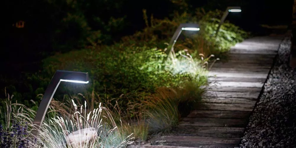 Gartenweg bei Nacht mit modernen, gebogenen Todus Saphira Gartenleuchten in Anthrazit, die den Pfad stilvoll beleuchten.